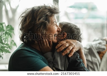 Grandmother and grandson spend time together, horizontal shot, the grandmother is no longer alone, smiling happily and hugging her little grandson