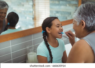 Grandmother helping granddaughter brush her teeth in the bathroom at home