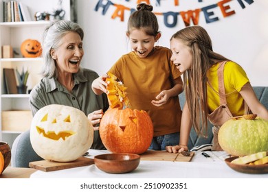 Grandmother and her granddaughters are having fun while carving pumpkins for halloween, creating festive decorations and enjoying quality time together - Powered by Shutterstock