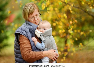 Grandmother With Her Infant Grandson In A Baby Carrier Having Fun Hiking In A Forest On Beautiful Autumn Day. Granny Taking A Walk With Her Grandchild. Carrying A Baby.