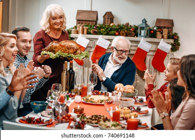 Grandmother Holding Christmas Turkey While Family Clapping