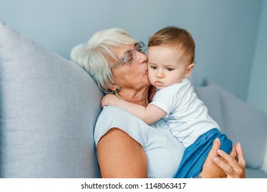 Grandmother Is Kissing Her Baby Grandson - Indoors Scene. Proud Grandmother Holding Baby Grandson. Senior Woman Hold Little Baby Boy. Multi Generation Family Playtime