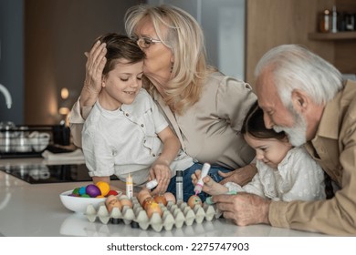 Grandmother kissing her grandsons head while they decorate Easter eggs with the family - Powered by Shutterstock