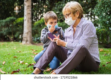 Grandmother and little kid playing with a smartphone in the backyard while wearing protective masks due to coronavirus outbreak