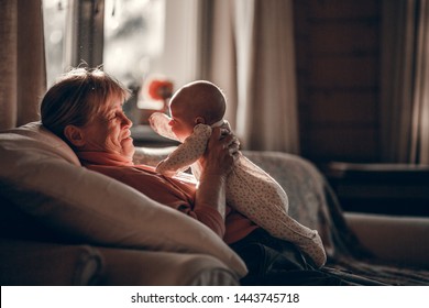 Grandmother Is Making Funny Faces To Newborn Her Grand Daughter.  Image With Selective Focus, Noise Effect And Toning.