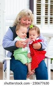 Grandmother Playing With Twin Babies While Sitting On Rocking Chair At Home On Porch