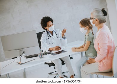 Grandmother With Protective Facial Masks With Cute Granddaughter At Black Female Doctor