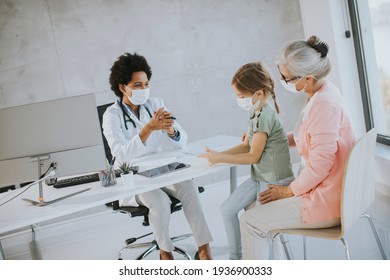 Grandmother With Protective Facial Masks With Cute Granddaughter At Black Female Doctor