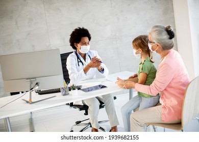 Grandmother With Protective Facial Masks With Cute Granddaughter At Black Female Doctor