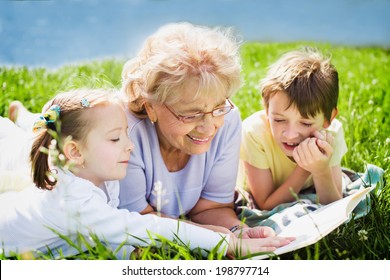 Grandmother Reading Book To Grandchildren Outdoors