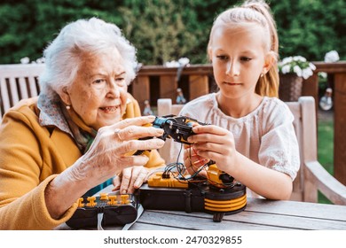 Grandmother supporting granddaughter in robotics, science, IT technologies and programming. Young girl assembling a simple robot and shoving it to grandma. - Powered by Shutterstock