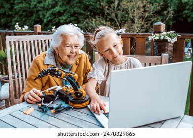 Grandmother supporting granddaughter in robotics, science, IT technologies and programming. Young girl assembling a simple robot and shoving it to grandma. - Powered by Shutterstock