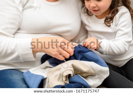 Grandmother teaches her granddaughter to mend clothes. Sustainability living, repairing clothes, shopping less concept.