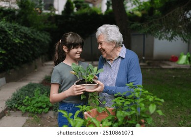 Grandmother teaching granddaughter to work in garden. Girl helping elderly grandma with plants, herbs and vegetables in garden, spending free summer time outdoor. - Powered by Shutterstock