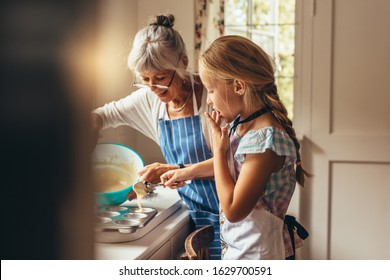 Grandmother teaching kid to make cup cakes. Happy grandmother and kid pouring cake batter in cup cake moulds.