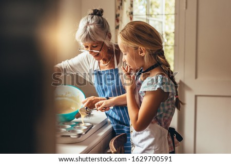 Grandmother teaching kid to make cup cakes. Happy grandmother and kid pouring cake batter in cup cake moulds.