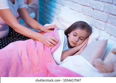 Grandmother Tucking In Granddaughter For Sleep In Bed At Night At Home.