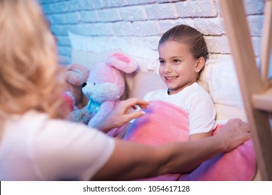 Grandmother Tucking In Granddaughter For Sleep In Bed At Night At Home.