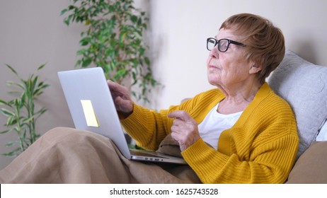 Grandmother Using Laptop Computer Relaxing In Bed. Computing Services For Retirees.