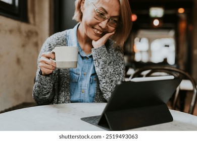 Grandmother in video call on digital tablet at cafe. Asian woman in video call on digital tablet. Senior asian woman watching video on tablet. Internet connection at cafe for senior woman. - Powered by Shutterstock