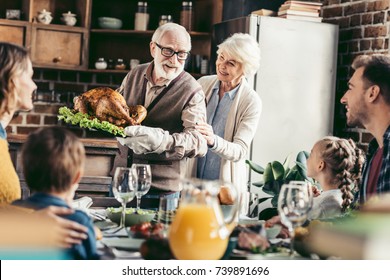 Grandpa With Delicious Turkey For Thanksgiving Dinner With Happy Family