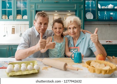 Grandpa, granddaughter and granny showing thumbs up while baking a pie. Happy times and memories, family portrait at a kitchen.