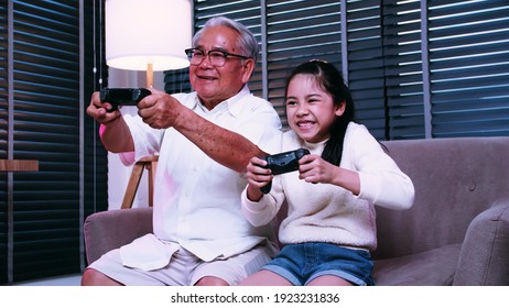 Grandpa And Granddaughter Are Having Fun Playing Video Games Together In The Living Room At Home.