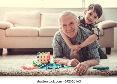 Grandpa and grandson are playing with toys, hugging, looking at camera and smiling while resting together at home