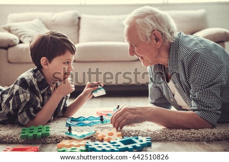 Grandpa and grandson are playing with toys, looking at each other and smiling while resting together at home