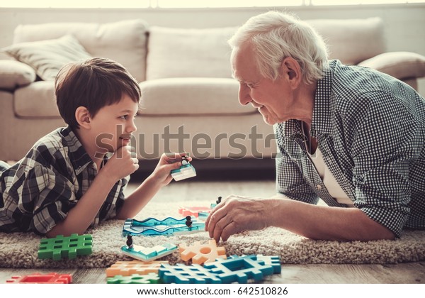 Grandpa and\
grandson are playing with toys, looking at each other and smiling\
while resting together at\
home