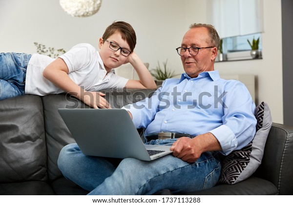 Grandpa sits with the grandson on\
the couch with the laptop and together they have great fun\
\

