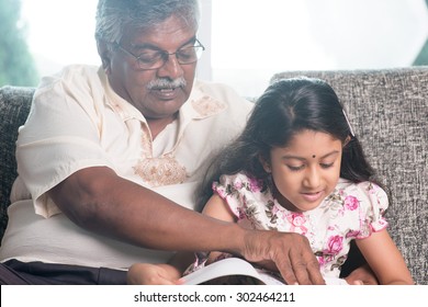 Grandparent And Grandchild Reading Story Book Together. Happy Indian Family At Home. Asian Grandfather And Granddaughter Indoor Lifestyle.