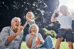 Grandparents, Bubbles And Children Play In Park Happy Together For Fun, Joy And Outdoor Happiness. Retired, Smile And Excited Elderly Senior Couple, Girl Grandkids And Love Playing Outside In Nature