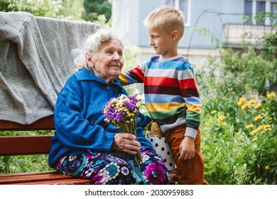 Grandparents Day, Reunited family, togetherness. Senior old grandma hugs grandson outdoors. Grandchild makes surprise for granny and gave her flowers