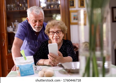 Grandparents Enjoy Making A Video Call On Their Cell Phone Sitting In The Living Room At Home