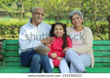 Grandparents enjoying with grand daughter in park surrounded with greenery and serenity. They are having joyful and cheerful time together in lush green environment. Loads of smile and happy moments.