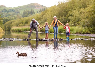 Grandparents With Grandchildren Crossing River Whilst Hiking In UK Lake District