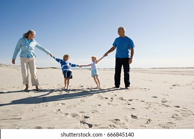 Grandparents And Grandchildren Holding Hands, Walking On Beach