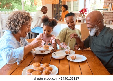 Grandparents With Grandchildren At Home Eating And Decorating Cakes With Family In Background - Powered by Shutterstock