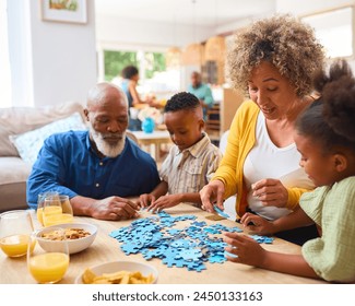 Grandparents With Grandchildren Indoors At Home Doing Jigsaw Puzzle With Parents In Background - Powered by Shutterstock