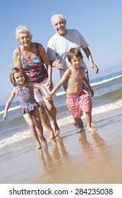 Grandparents And Grandchildren Running Along Beach