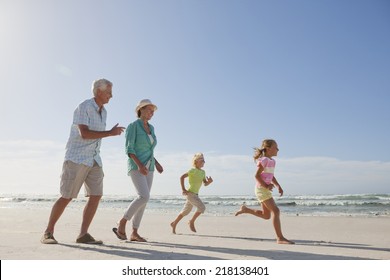 Grandparents And Grandchildren Running On Sunny Beach