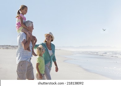 Grandparents And Grandchildren Walking On Sunny Beach