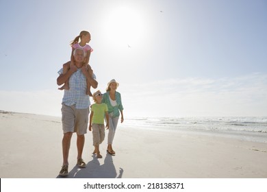 Grandparents And Grandchildren Walking On Sunny Beach