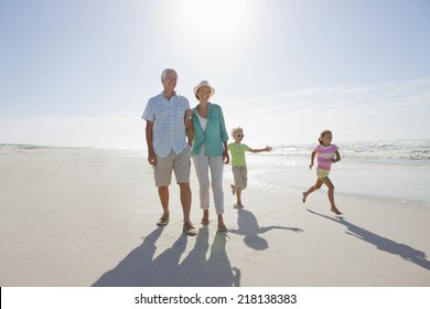 Grandparents And Grandchildren Walking On Sunny Beach