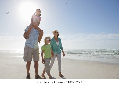 Grandparents And Grandchildren Walking On Sunny Beach