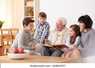 Grandparents And Grandchildren Watching Family Photo Album In Living Room