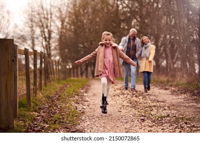 Grandparents With Granddaughter Outside Walking Through Winter Countryside