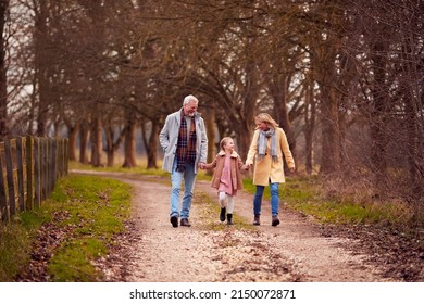 Grandparents With Granddaughter Outside Walking Through Winter Countryside Holding Hands