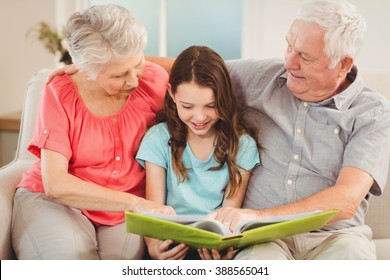 Grandparents and granddaughter sitting on sofa and reading a book with granddaughter - Powered by Shutterstock